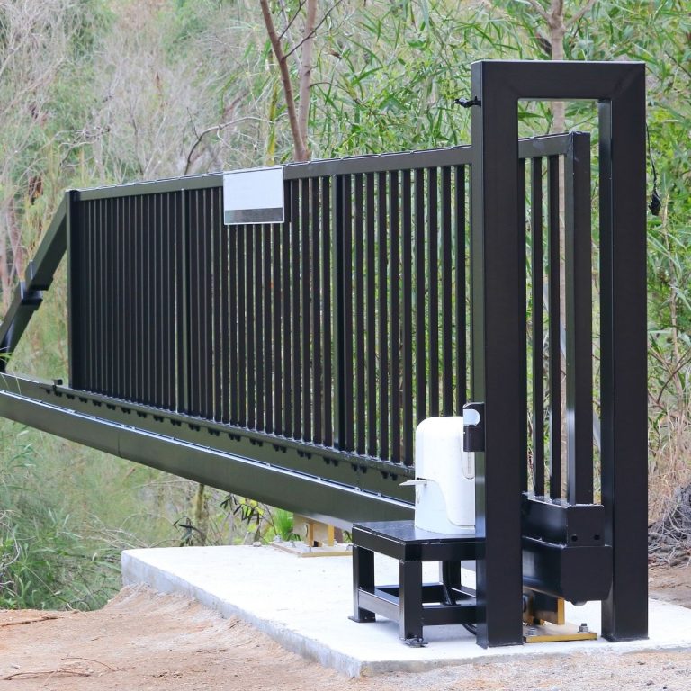 Black sliding driveway gate on its track with the drive motor beside it