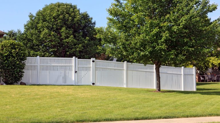 White vinyl fence with an open picket top section beside mature trees